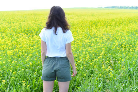Russian woman standing in rapeseed field and looking away. back viewの写真素材