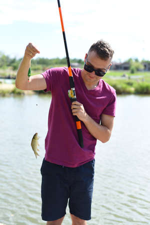 Young fisherman holding crucian carp on fishing rod against a pondの写真素材