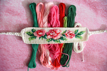 Woven DIY friendship bracelet with bright flower pattern Rose near skeins of embroidery thread