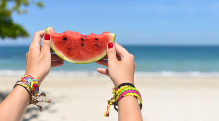 Womens hands with friendship bracelets holding watermelon against beachの写真素材