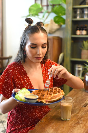 Young woman eating waffles in a coffee shopの写真素材