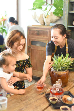 Vietnamese waitress serves hot tea for mother with daughter in cafeの写真素材