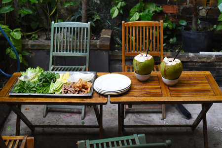 Traditional Vietnamese meal greens roasted meat with rice paper and coconut drinks on wooden tableの写真素材