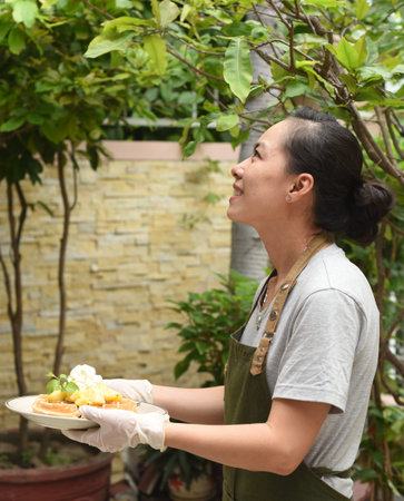 Vietnamese woman waitress serving Belgian waffles with fruits and ice cream in outdoor cafe looking...