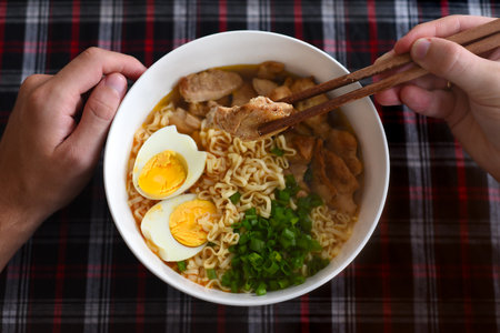 Piece of chicken in chopsticks with japanese ramen and males handsの写真素材