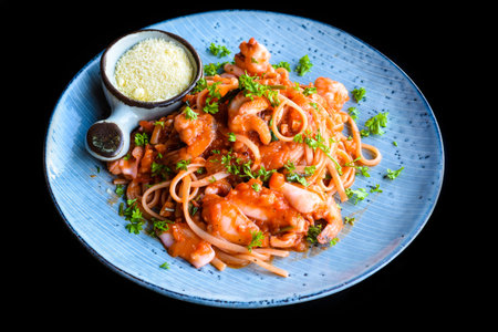 Pasta carbonara with sea food on blue plate isolated on black background side view