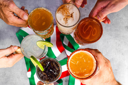 Hands holding mexican drinks making clink against mexican flagの写真素材