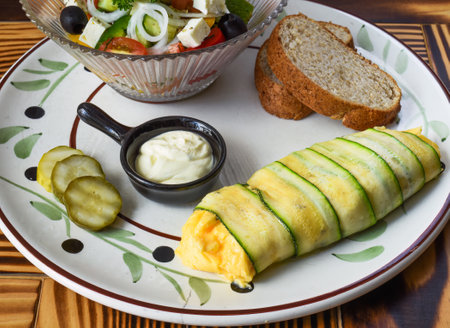 Zucchini omelette with fresh salad, bread and sauce on a plate on wooden tableの写真素材
