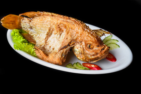 Fish grilled in batter with vegetables and greens on white plate isolated on black background side viewの写真素材