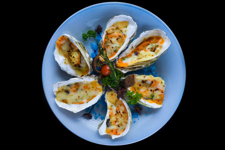oysters baked with cheese on plate with blue salt isolated on black top viewの写真素材