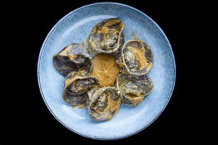 Ravioli with chicken and mushrooms inside and grated cheese on blue plate isolated on black backgroundの写真素材