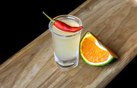 Alcohol shot made of orange juice and chili on wooden board with with copy spaceの写真素材