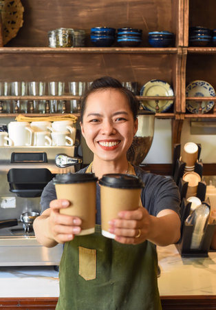 Vietnamese smiling waitress holding paper cups with coffee in a cafeの写真素材