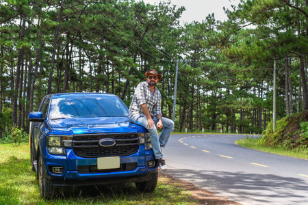 Young man sitting on his blue car in the forest