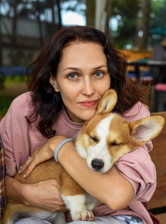 Portrait of beautiful young brunette woman holding her corgi dog and looking at cameraの写真素材