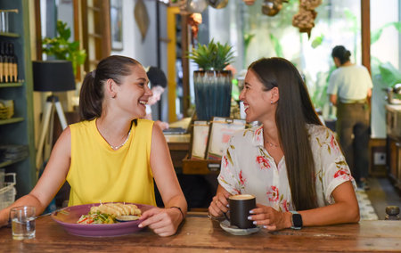 Two best friends talking and eating in a cafeの写真素材