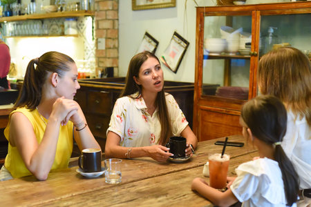 Female best friends talking and eating in a cafeの写真素材