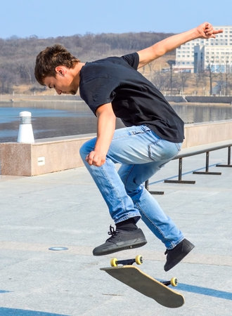 Young Russian skater in black t-shirt and blue jeans jumping on the skateboard on a early spring day