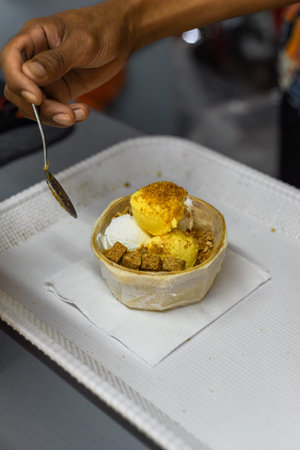 Hand holding coconut and mango ice cream in coconut shell in Jalan Alor street food market in Kuala...