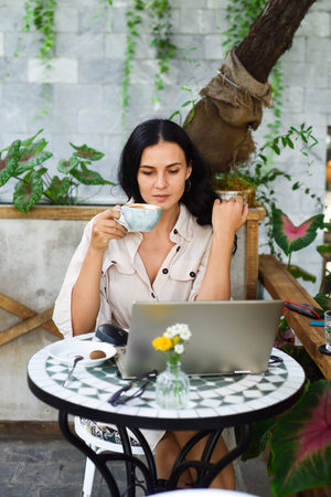Young ukrainian brunette woman freelancer working with laptop and drinking coffee in cafeの写真素材
