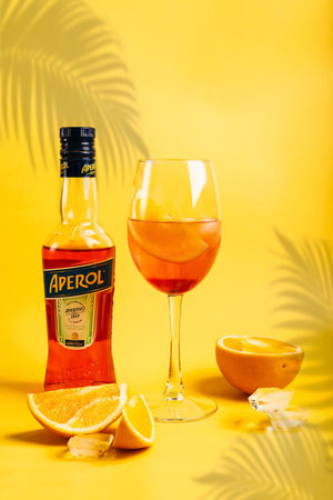 Bottle of Aperol Aperitivo summer cocktail drink with glass with spritz cocktail and oranges on bright yellow backgroundのeditorial素材