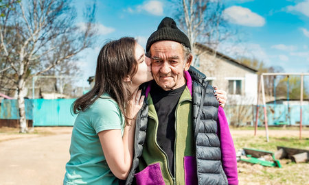 Portrait of granddaughter kissing in cheek her 75 years old grandfather in russian villageの写真素材