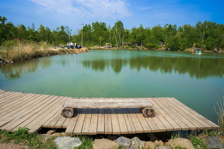 Landscape with wooden pier and bench near pond for fishing, summer activities