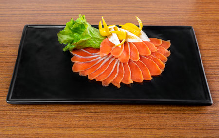 slicing appetizer of red fish slices on a black plate on a wooden table top viewの写真素材