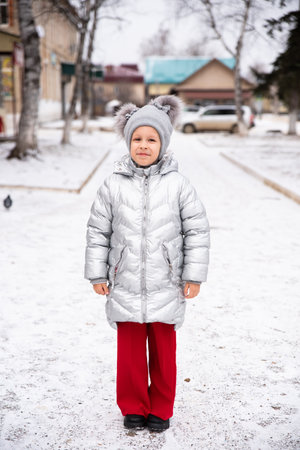 8-year-old Russian girl smiles in the snow, wearing a warm winter jacket and hat. She stands outdoors in a snowy landscape, looking at the camera with a joyful, playful expressionの写真素材