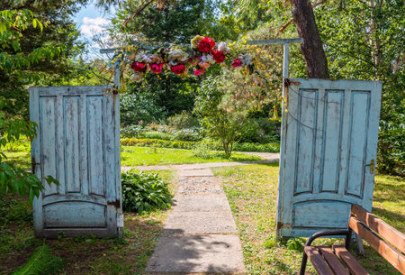 A creative garden entrance made of two old decorative doors forming an archway, adorned with flowers. The setting highlights creativity, upcycling, and handmadeの写真素材