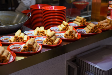 Stacked crispy pancakes with sauce on plates, Chinese street food in Shanghai. Evening time, many identical portions arranged in rowsの写真素材