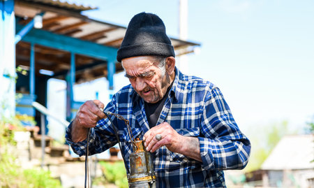 Elderly Russian man in a rural village holding a drainage pump with both hands, checking equipment under the open skyâsimple village routine in retirementの写真素材