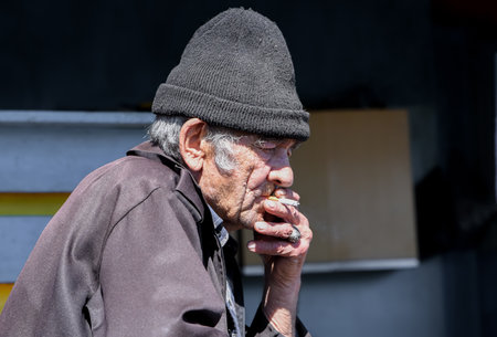 Elderly Russian village man lost in thought, smoking a cigarette in solitude, reflecting on life with a melancholic, distant gazeの写真素材