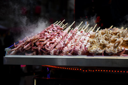 Night street food market in Shanghai, China. Grilled seafood skewers octopus and tentacles sizzling on fire. Dark, atmospheric vibe.の写真素材