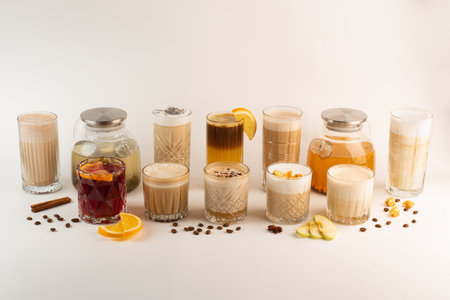 A variety of autumn drinks in glasses, including coffee, tea, and mulled wine, arranged in a row on a white backgroundの写真素材