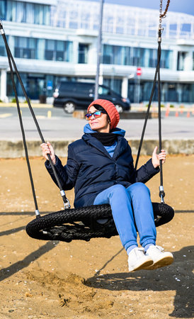 Russian woman about 50 years old swinging on a playground swing at the beach in Primorsky Krai, Russia, enjoying a sunny autumn day with nostalgic mood.の写真素材