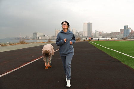Two women, aged 50 and 60, in tracksuits, run around a stadium.