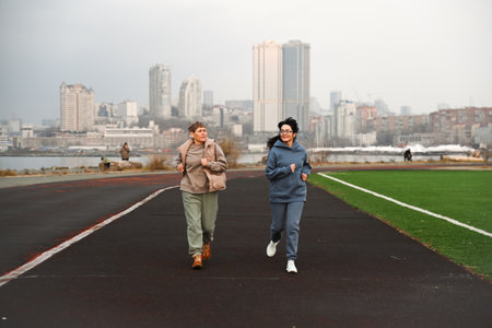 Two women, aged 50 and 60, in tracksuits, run around a stadium.の写真素材