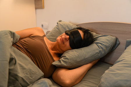 Calm 50 year old woman sleeps on her side wearing a sleep mask, expressing quiet rest, inner peace, comfort and a soothing mindful atmosphere.の写真素材