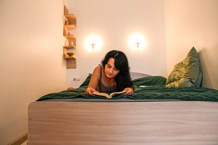 Russian 50 year old woman reading in bed enjoying a calm mindful moment focusing on personal growth relaxation emotional balance and quiet evening restの写真素材