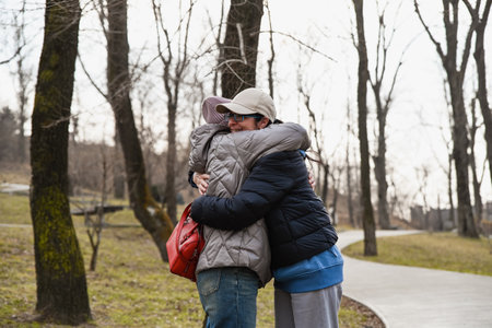 Two women 50 years old and 60 years old embrace closely in a spring park, showing emotional warmth, mindfulness, trust and a peaceful moment of friendship.の写真素材