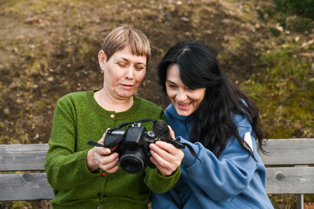 Two Russian women in their 50 years old and 60 years old share a joyful moment reviewing photos, showing mindfulness, creativity, active aging and warm friendship.の写真素材