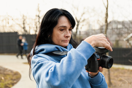 A 50 year old Russian woman adjusts her camera in a park, enjoying her photography hobby with calm focus and a sense of creative freedom.の写真素材