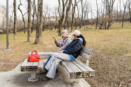 Two Russian friends aged 50 and 60 sit in Nagorny Park Vladivostok, enjoying calm spring conversation that supports emotional balance, connection and wellbeing.の写真素材