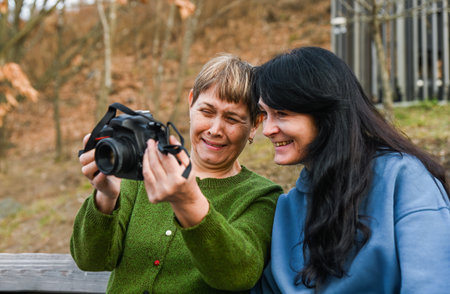 Two women in their 50s and 60s laugh together while enjoying photography, showing mindfulness, freedom, active aging and creative joy.の写真素材