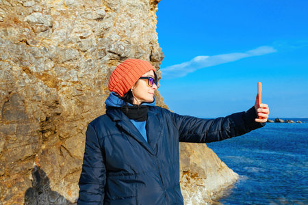 Russian woman taking selfie near the Sea of Japan coast in Vladivostok during a cold sunny day. Concept of travel blog, solo trip, and seasonal adventure.の写真素材