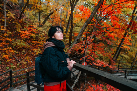 Russian woman 50 years old solo traveler looking into distance at autumn leaves on forest stairs Far...