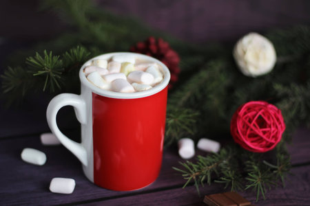 Mug filled with hot chocolate and marshmallows with christmas tree as the backgroundの写真素材