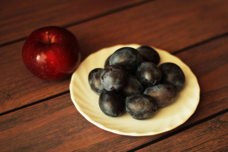 plums on a plate and red apple with wooden backgroundの写真素材