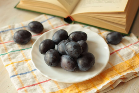 plums on a plate with dish cloth, book and wooden backgroundの写真素材